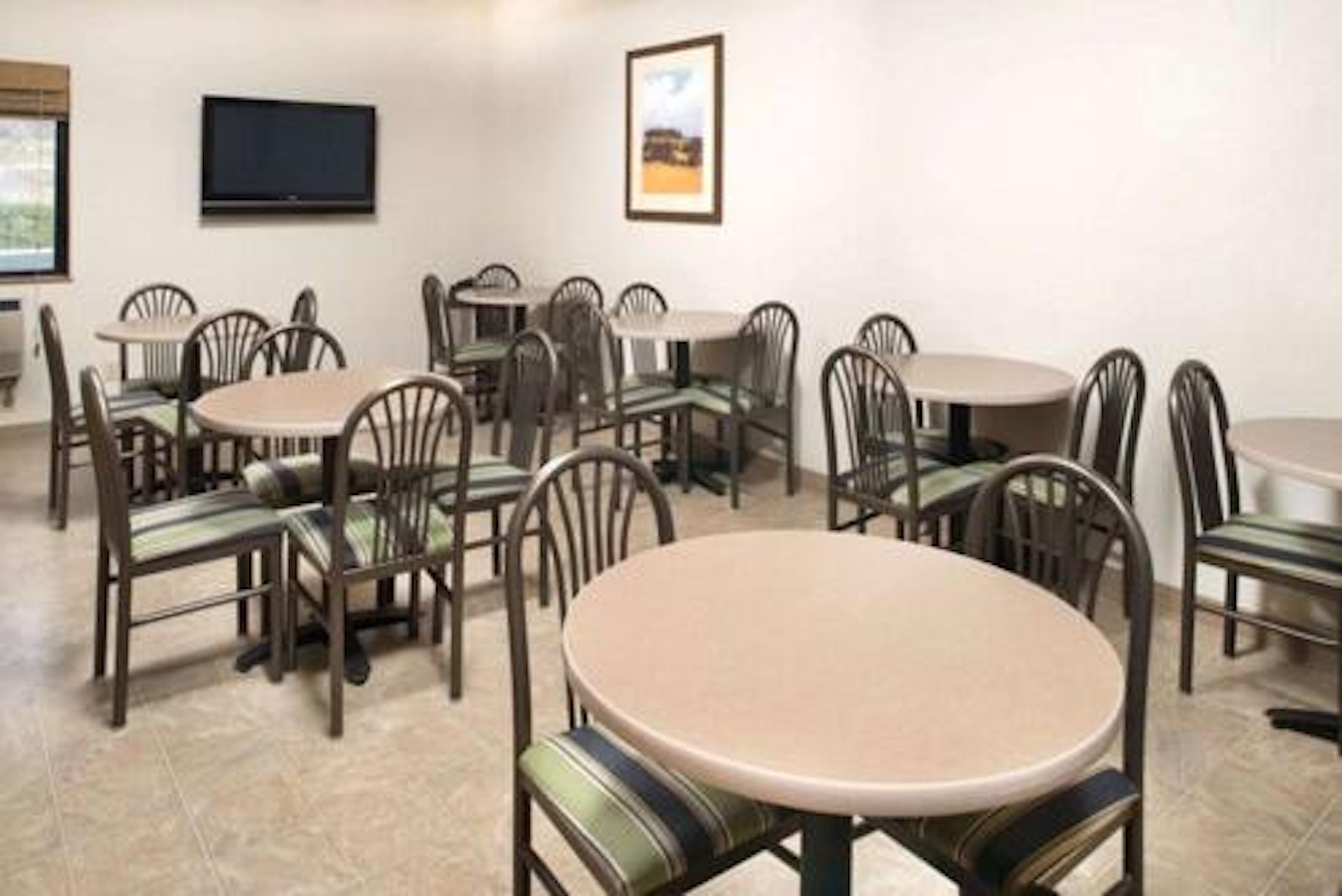 Small breakfast area with round tables, striped chairs, and a wall-mounted TV.