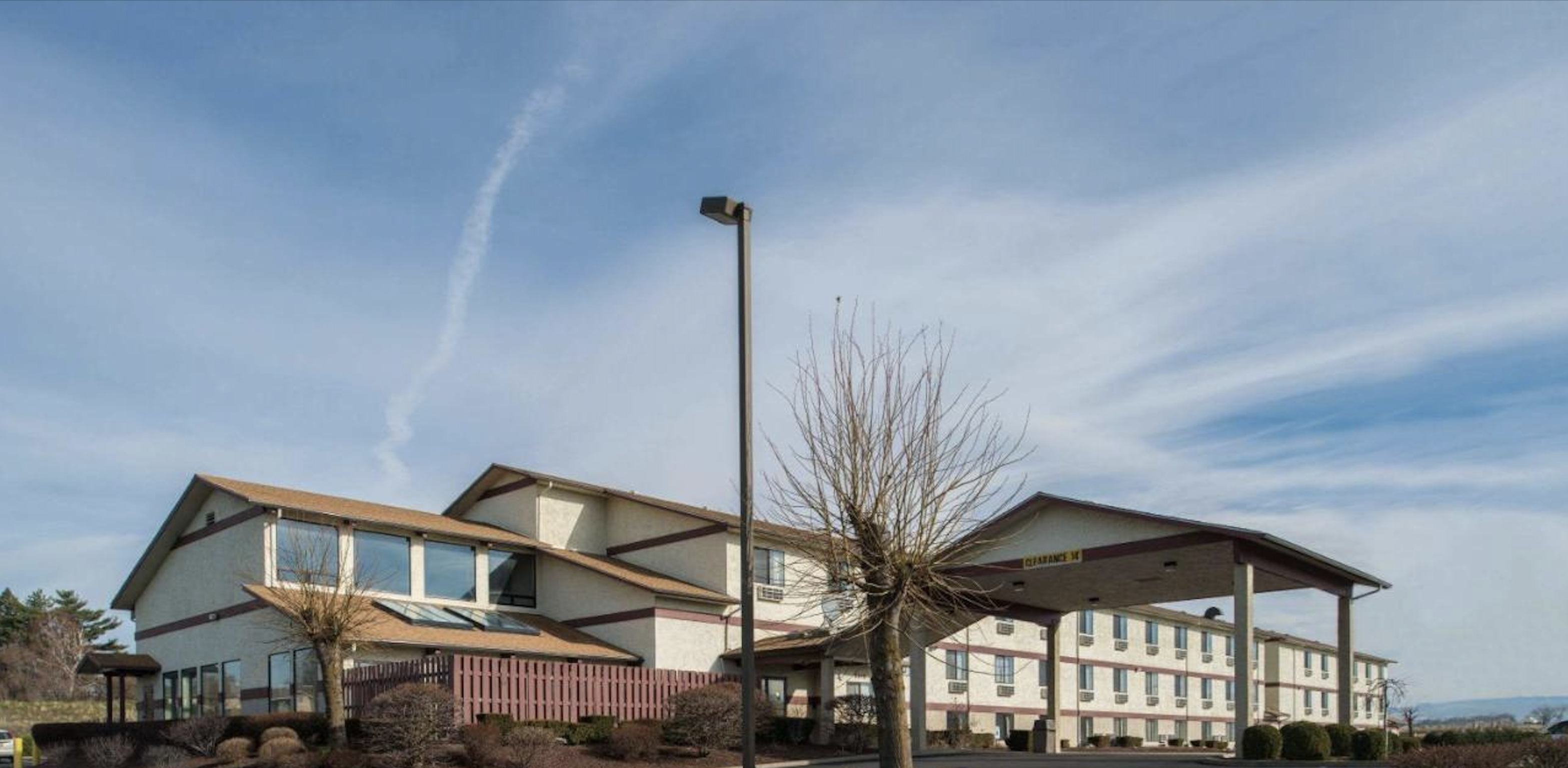 Exterior of a two-story hotel with a drive-up canopy and trimmed landscaping under a partly cloudy sky.