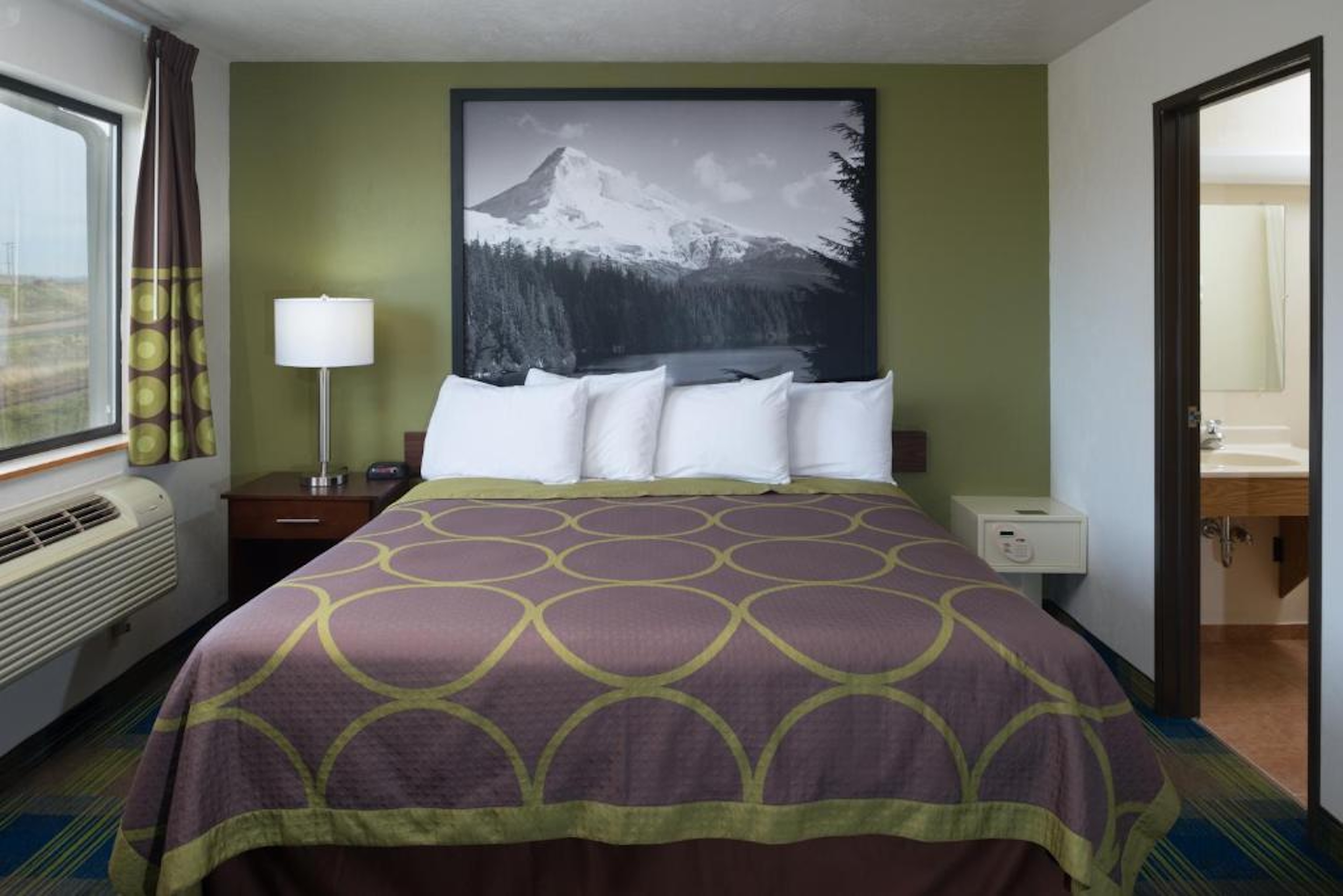 Hotel room with a large bed, mountain-themed wall art, and green accent wall.