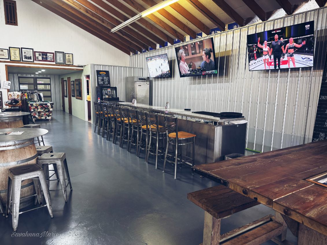 Industrial-style bar area with metal stools, TVs, and wood barrel tables.