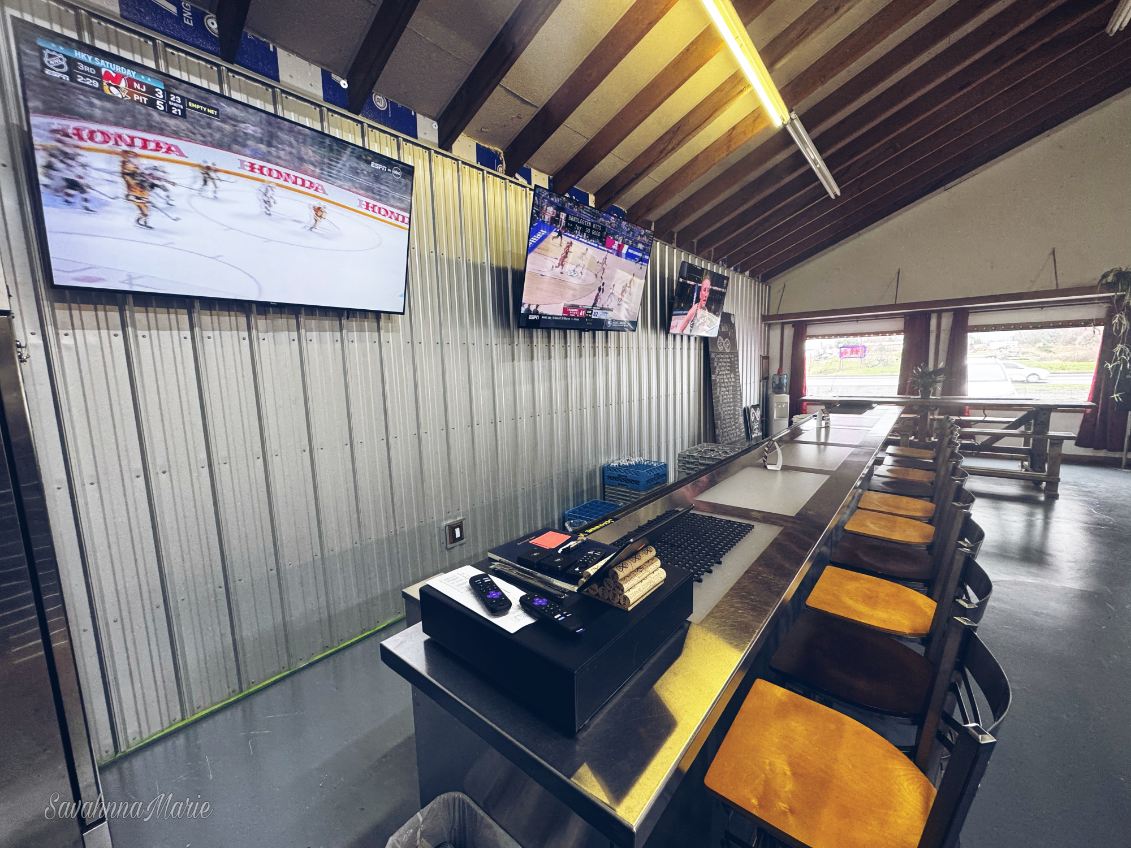 Bar counter with mounted TVs playing sports and a view of the outdoor lot.