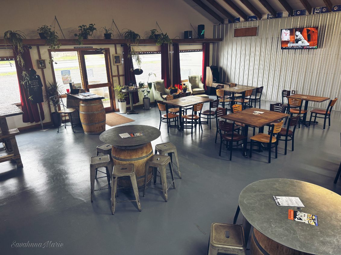 Spacious seating area with wooden tables, barrel decor, and wall-mounted TV.