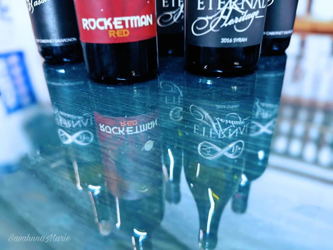 Close-up of wine bottles with brand labels reflected on a shiny surface.