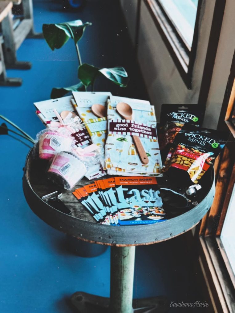 Round table with gift items, snacks, brochures, and a plant by the window.