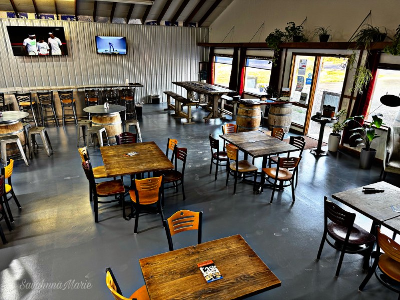 Spacious indoor dining area with wood tables, barrel tables, and large windows letting in natural light.