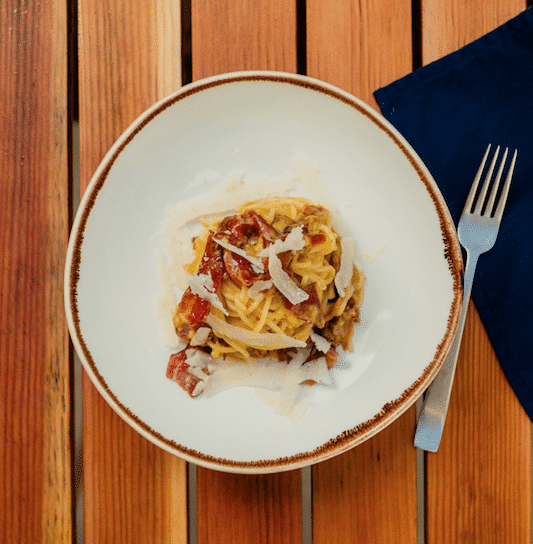 White bowl filled with pasta, bacon and cheese on a wood table